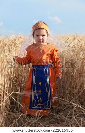 Little girl in a national Armenian dress costs among wheat field