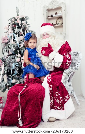 little girl in a beautiful blue dress sits on a lap at Saint Nicolas about a New Year tree