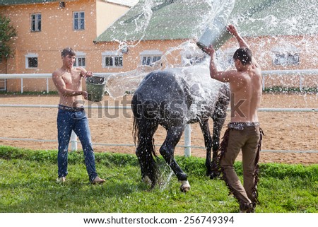 Two young men wash a horse and pour over each other water from buckets
