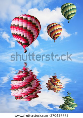 Three big balloons in the blue sky are reflected in water