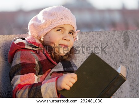little happy girl reads the book on the street