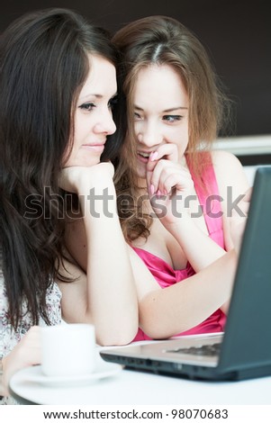 Two girls work on a laptop, sitting in cafe in shopping center