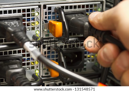 Technician / engineer inserts power cord into a rack server in the second power supply for redundancy. Shot in sa data center.
