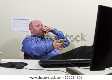 A businessman / office worker celebrating achievement with a cigar and congac at the office.