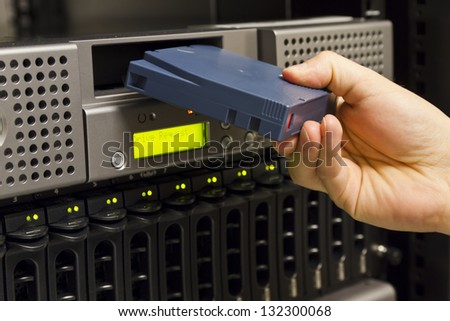 A close-up of a IT engineer / technician insert a backup tape in a backup robot in a rack. Shot in a data center.