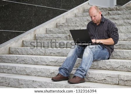 A businessman working with his computer / laptop in stairs outside. Seems focused and happy.