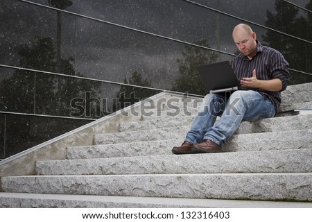 A questioning and frustrated man working with his computer / laptop in stairs outside.
