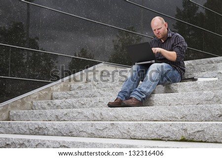 A student / businessman try to find a solution on his computer / laptop in stairs outside.