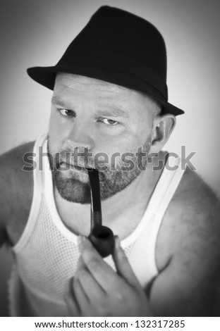 Man smoking tobacco pipe, with hat and singlet.