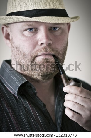 Man smoking tobacco pipe, with hat and singlet.