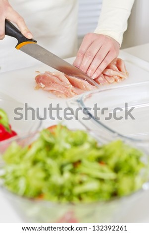 Young woman in a white kitchen cut chicken meat fillet. Vegetables.