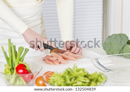 Young woman in a white kitchen making a chicken meat fillet dish.