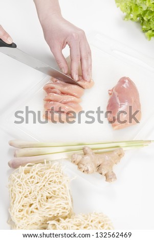 Young woman in a white kitchen making a chicken meat fillet dish with vegetables, ginger and pasta / noodles.