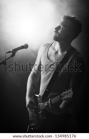 Black and white photo of a young man playing rock concert. sings and play guitar.