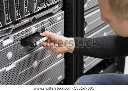 A IT engineer / technician / consultant insert a backup tape in a backup robot in a rack. Shot in a data center with blade servers and disk enclosures.
