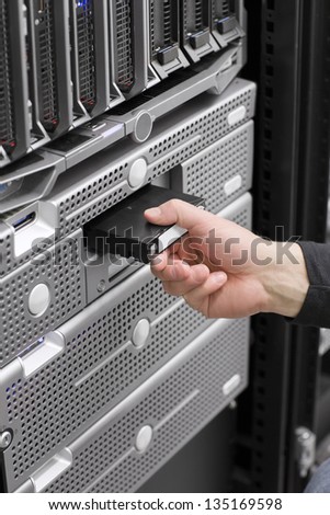 A IT engineer / technician / consultant insert a backup tape in a backup robot in a rack. Shot in a data center with blade servers and disk enclosures.