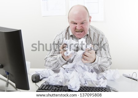 Overworked, Frustrated and Angry Businessman. Angry and overworked office worker with a heap of paper at the office desk. To much work.