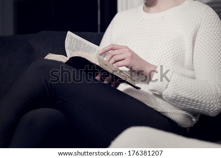 Girl reading the holy bible at home. Sitting in sofa.