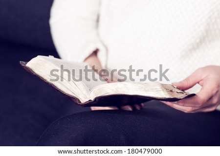 Christian woman reading the holy bible at home. Sitting in sofa.