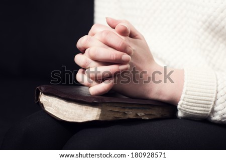 Woman folding hands over her holy bible and praying to God.