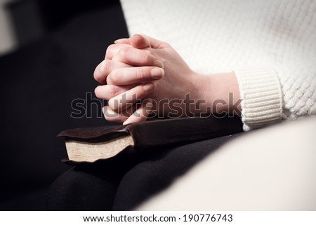 Praying woman folding hands over bible