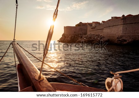 Old Sailing Ship Sails Into The Sunset Next To The City Walls Of Dubrovnik