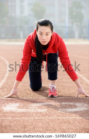 Athletic Chinese woman in start position on track