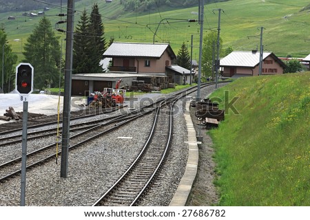 Railroad tracks with electricity poles leading through a village in the alps