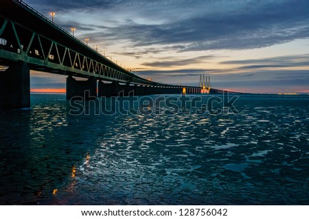 The Oresund Bridge is reflected in icy waters on a cold winter evening. The bridge, with trains running on the lower level and cars on top, connects Sweden to Denmark.