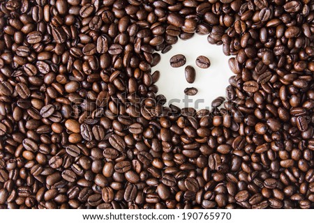 Coffee beans on a white background with a face made from coffee beans in the upper right hand corner of the image.