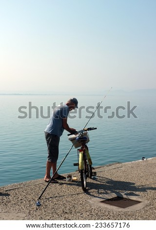 AKCAY, TURKEY- AUGUST 15, 2014:  Elderly man parks his bike and gets ready to angle on concrete pier in Akcay, Turkey