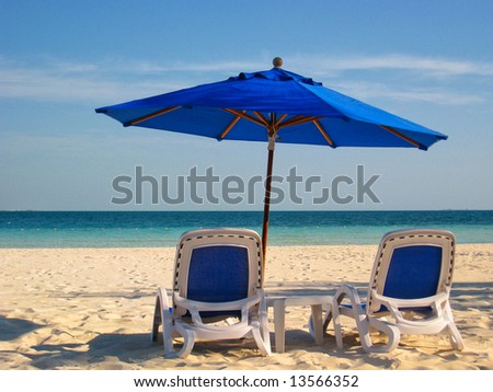 Two lounge chairs under a blue umbrella on the white sandy beach