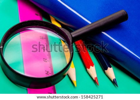 Colorful pencils, lens, book, and ruler on colored paper.