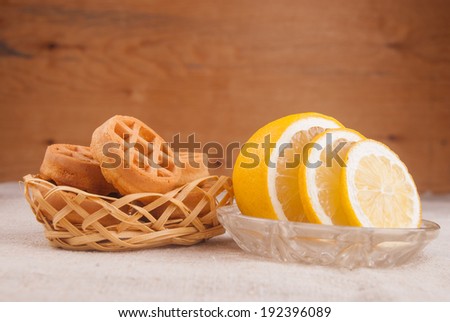 Macro shot of lemon cut to slices on little plate and waffles in basket on table covered with rough textile