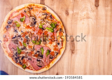 pizza with mozzarella,  ham, mushrooms chicken, broccoli, and tomatoes, whole, uncut, on wooden table