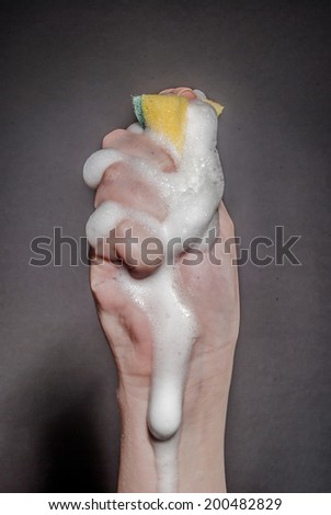 Female hand squeezing sponge with foam against black background