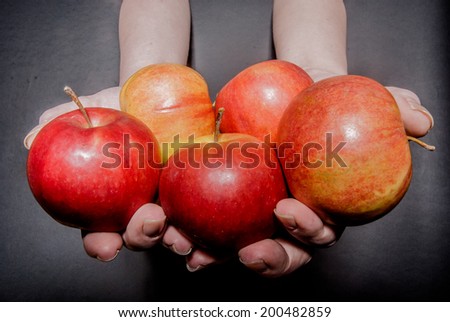 Female hands holding five red apples against black background