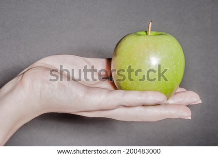 Female hand holding green apple against black background as a metaphor for concepts of health, life, and ideas