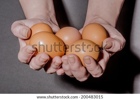 Female hands holding five brown eggs against black background