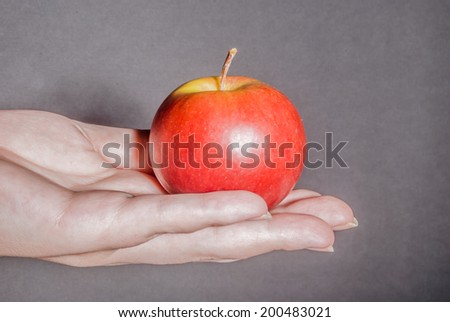 Female hand holding red apple against black background as a metaphor for concepts of health, life, and ideas