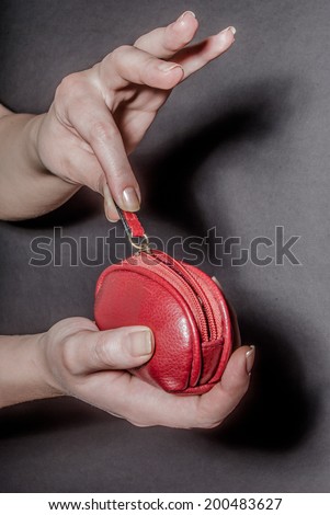 Female hand holding red wallet with zipper filled with money, against black background