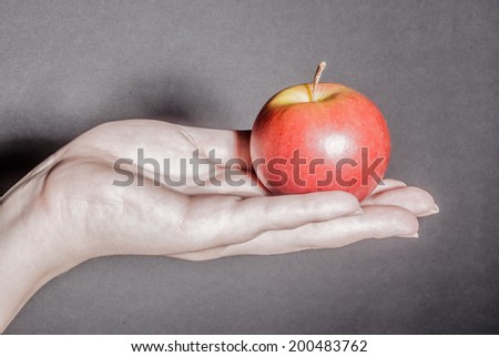 Female hand holding red apple against black background as a metaphor for concepts of health, life, and ideas