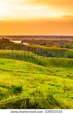 Sunset in countryside. Colorful landscape with trees, hills, river and cloudscape