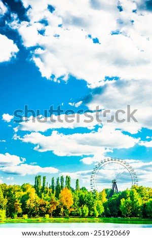 Big ferris wheel in city park. Beautiful landscape with lake, trees blue sky, and clouds
