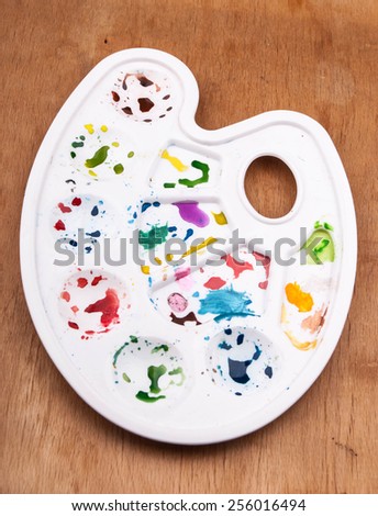 White plastic art palette with random watercolor paint blobs on wood