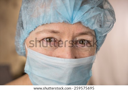 Female doctor wearing medical mask and surgical cap looking at patient and smiling