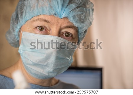 Female doctor wearing medical mask and surgical cap looking seriously and worried at patient with computer in background