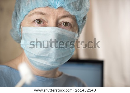 Closeup of female doctor wearing medical mask and surgical cap looking seriously and worried at patient