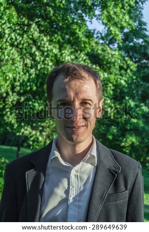 Young man in formal outfit looking with smile in camera, outdoors on the green background. Business man in a green zone or park. An image for topics of finance and business.