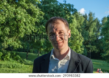 Young man in formal outfit looking with smile in camera, outdoors on the green background. Business man in a green zone or park. An image for topics of finance and business.
